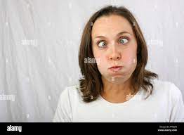 Cute brunette 20s 30s young woman puffs her cheeks crosses her big blue  eyes to make an ugly funny humorous facial expression Stock Photo - Alamy