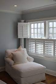 This serene gray bedroom features white walls framing large patio windows finished with white plantation shutters as hardwood floors are covered with a gray geometric rug sat below a bed dressed in gray pebble bedding accented by a charcoal gray upholstered headboard. Windows With White Shutters In Bedroom Gray Bedroom Walls Blinds For Windows Living Rooms Home