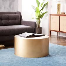 This contemporary piece sits on a circular metal drum base with a gold finish and lower shelf. Metal Drum Antique Brass Coffee Table