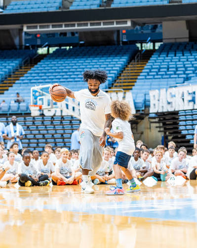 Coby White dribbling alongside a camper at the Dean E. Smith Center