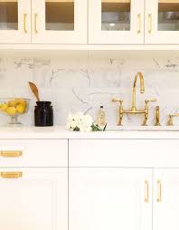 There Is A Lovely Disparity In This Kitchen Between The Marble Accents And The Gold Hardware The Bea Gold Kitchen Gold Kitchen Hardware White Kitchen Cabinets