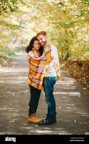 Beautiful couple man woman in love. Boyfriend and girlfriend wrapped in  yellow blanket hugging standing outdoor in park on autumn fall day.  Togetherne Stock Photo 