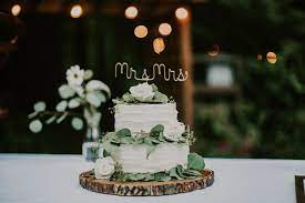 Two Teir White Wedding Cake On A Wood Round With Eucalyptus And White Rose Decoration Mr Mrs Gol One Teir Wedding Cake Dream Wedding Cake Wedding Cake Table