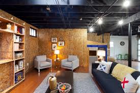The exposed ceiling joists are painted a deep charcoal, the concrete floor is a fun red, and wood shelving and furniture add interest and utility. Style Of Painting Basement Ceiling Black Ideas