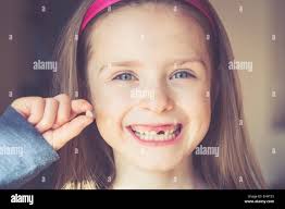 Portrait of smiling little girl with tooth gap holding milk tooth in her  hand Stock Photo