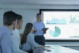 Businessman Making Presentation Using Screen Of Charts And Graphs In D943_247_853