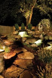 Cascading Waterfalls With Glowing Lights Flow Through This Rock Garden Creating A Calm Outd Landscape Lighting Solar Landscape Lighting Landscape Lighting Kits