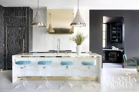 White paneled floor with a white kitchen island, broke cleverly by the wood and metal set of bar stools. White Marble Waterfall Kitchen Island With Lucite Barstools Contemporary Kitchen