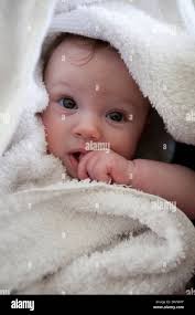 Baby wrapped in white towel, fingers in mouth Stock Photo