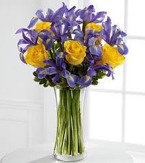 A Tall Presentation Of Full Blooming Blue Iris Yellow Roses And Simple Greenery In A Tall Clear Glass Vase Iris Bouquet Flowers Bouquet Flower Arrangements