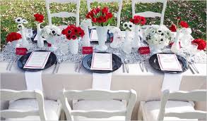 A beautifully decorated table has every element balance each other as is seen in the red and white striped ribbon twined through a spray of pine needles, pinecones, and berries that matches the red and white stripes of the table runners and the red candleholders and white candles. Black White And Red Vintage Art Deco Bridal Shower Ideas Red Wedding Decorations White Wedding Decorations Black Wedding Table