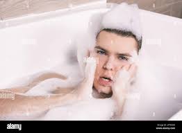Funny sexy guy poses in the bathtub completely in foam Stock Photo