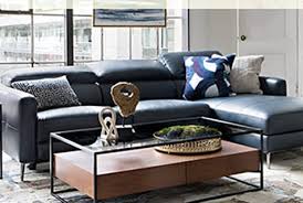 A glass and stained wood coffee table with candles on a tray, a gold vase with a floral arrangement, a bowl with balls and books. How To Style A Coffee Table Tabletop Decor Ideas Living Spaces