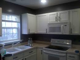 This design features white kitchen cabinetry with dark granite countertops throughout the room with the exception of the island counter which is dark grey and with a white worktop surface. Black Wall With White Cabinets Novocom Top