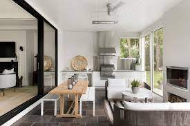 Sunroom dining room features a vaulted cieling adorned with an oly studio muriel chandelier illuminating a round gray stone top dining table lined with white and gray print dining chairs atop a. Sunroom With Kitchen And Fireplace Transitional Living Room