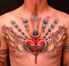 In some designs, the sacred heart is colored, usually red and gold, so that it becomes the main focus of the tattoo. Sacred Heart With Ribbon Tattoo On Man Chest