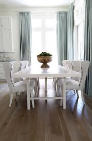 A Glossy White Lacquered Dining Table Is Lined With White Linen Wingback Dining Chairs Sur Wingback Dining Chair Transitional Dining Room Lacquer Dining Table