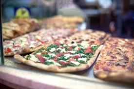 Pizza al taglio or pizza al trancio (italian for pizza by the slice — literally by the cut) is a variety of pizza baked in large rectangular trays, and generally sold in rectangular or square slices by weight, with prices marked per kilogram or per 100 grams. So Bestellen Sie Pizza Im Pizza Al Taglio Shop In Italien