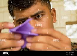 Staff Sgt. Ismael Esconde, a cyber system chief of 3d Marine Regiment  demonstrates how to fold an origami paper crane from a piece of purple  paper to the children of Mokapu Elementary