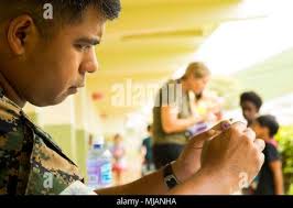 Staff Sgt. Ismael Esconde, a cyber system chief of 3d Marine Regiment  demonstrates how to fold an origami paper crane from a piece of purple  paper to the children of Mokapu Elementary