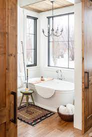 An airy primary bathroom showcases a dual sink vanity and a chaise lounge facing the freestanding bathtub by the arched window lighted by a crystal chandelier. Chandelier Over Tub Ideas Photos Houzz