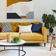 A mustard yellow sofa accented with red and white pillows sits on a diamond pattern jute rug facing a clear acrylic coffee table and beneath a tree art piece. Ideal Home A Mustard Yellow Sofa Paired With Modern Facebook