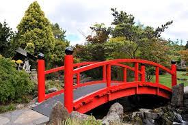 The Pattern Of The Stone Walkway Gives Way To A Sturdy Tread Over Wooden Planks The Bold Red Rail Japanese Garden Design Backyard Landscaping Designs Backyard