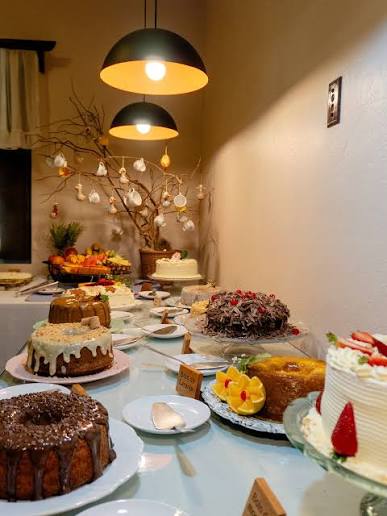 Mesa com tortas artesanais, fatias de bolo decoradas e cafés com arte no leite