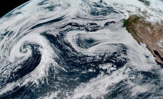 Satellite imagery showing shifting ocean temperatures and heavy storm clouds gathering over the Pacific Coast.