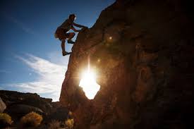 A silhouette of man climbing on rock, mountain at sunset. Man Climbing Rock Against Sky On Sunny Day Stockphoto