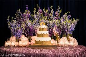 Beautiful white wedding cake with flowers on a round table near his green twig and plate with forks. Magnificent Indian Wedding Cake Table Decor Photo 243117