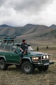 Young Man Sitting On The Old Green Jeep Parked In Wild Area Stocksy United Green Jeep Overland Vehicles Toyota Land Cruiser