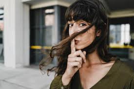 Smiley face with finger in mouth descripstion. Portrait Of Smiling Brunette Woman Finger On Mouth Stockphoto