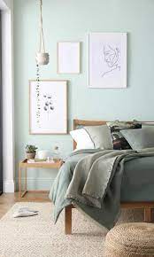 Satin pillows on a minimalist bed by a white empty wall in a trendy bedroom interior with gray and teal green decorations. 25 Soothing Green Bedroom Decor Ideas Shelterness