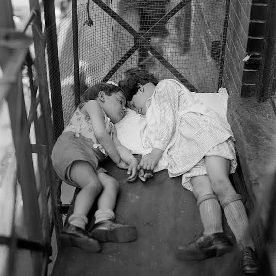 NEW YORK, 1938 — FIRE ESCAPE DREAMS High above the street, where the city  never truly slept, a group of Italian immigrant children lay huddled  together on a fire escape. Their small