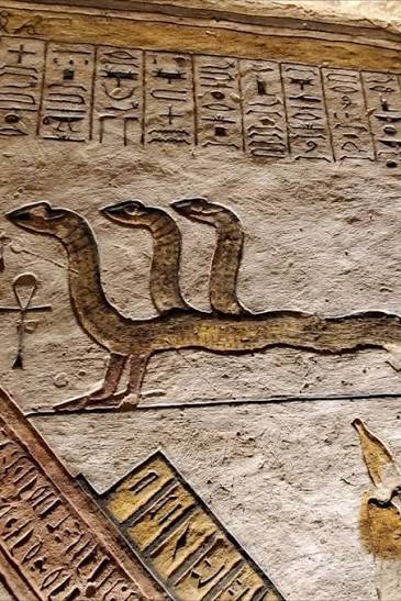 الثعبان ذو الثلاثة رؤوس: حارس الأسرار في العقيدة المصرية القديمة تُظهر هذه الصورة نقشًا جداريًا نادرًا من مصر القديمة، يحتوي على ثعبان بثلاثة رؤوس تحته صفوف من الرموز الهيروغليفية الدقيقة. هذا الكائن