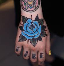Traditional Style Blue Rose Tattoo On The Right Hand And A Word Fake On The Fingers Rose Hand Tattoo Traditional Hand Tattoo Traditional Rose Tattoos