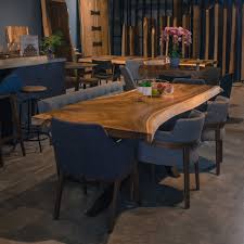 A brown kitchen with hardwood floors, wooden cabinetry, and kitchen counters along with a center island with breakfast bar paired with wooden chairs. Suar Wood Dining Table Masons Home Decor