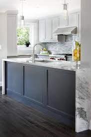 Two Modern Light Pendants Hang Over A Dark Blue Wainscoted Kitchen Island Topped With A Gray And Wainscoting Kitchen Blue Kitchen Island Kitchen Cabinets Decor