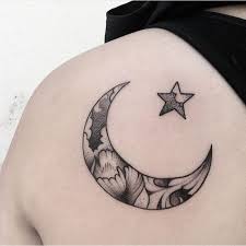 A crescent moon creates the centerpiece of this tattoo and is embellished with a feather, multiple stars, and a few nonsensical designs. Black And Grey Moon And Star Tattoo On Left Back Shoulder