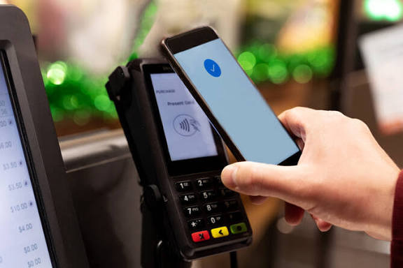 Consumer tapping a smartphone wallet at a contactless terminal during checkout