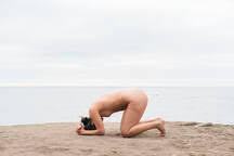 Nackte junge Frau kniend auf Sand am Strand gegen den Himmel, lizenzfreies  Stockfoto