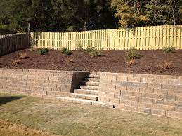 Fountain on deck in front of a retaining wall with steps leading to the upper landscape. Admin Landscaping And Retaining Walls Between The Edges Landscaping Retaining Walls Sloped Backyard Backyard Retaining Walls