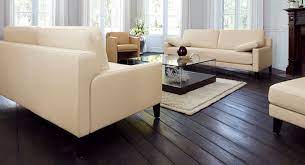 The living area has dark cherry wooden floors, light cream wallpapered walls, white ceiling and some light beech wood accents. Ivory Color Couches Dark Wooden Floor White Flowers Glass Coffee Table Dark Wooden Floor Living Room Designs Modern Room