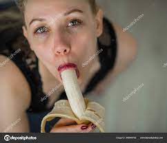 A blonde in black lace lingerie seductively sucks and licks a banana. Woman  with sensual red imitates oral pleasure. Stock Photo by ©inside-studio  346948752