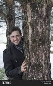 Playful couple hiding behind a tree trunk in the snow looking into the camera. Man Hiding Behind Tree Image Photo Free Trial Bigstock