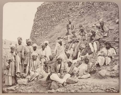 Photograph of the Khan of Lalpura, the leader of the Lalpura region of Afghanistan, and his followers on a mountainside. The Khan is standing in the middle of a group of Afghan