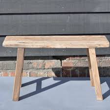 A simple sturdy outdoor bench of thick logs and planks of reclaimed wood with a natural finish. Reclaimed Small Rustic Trestle Bench In Solid Elm