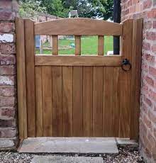 A wooden garden gate amid green spring growth with trees and a picket fence behind. Made To Measure Hardwood Gates Buy Online Based In Manchester Village Products