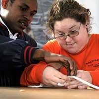Boatswain's Mate 2nd Class Jamie Marriott helps a student from the  LifeSkills Learning Center tie a square knot.